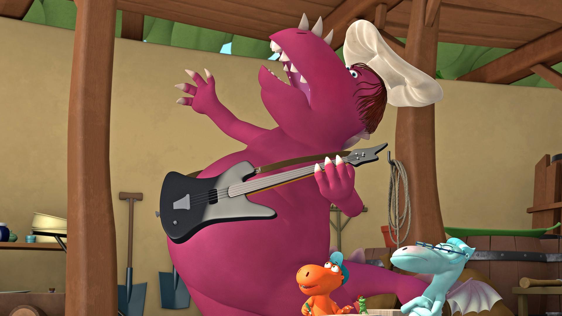 Der Chefkoch spielt E-Gitarre, während Kokosnuss begeistert zu ihm aufblickt. Ein blauer Drache steht mit verschränkten Armen daneben.