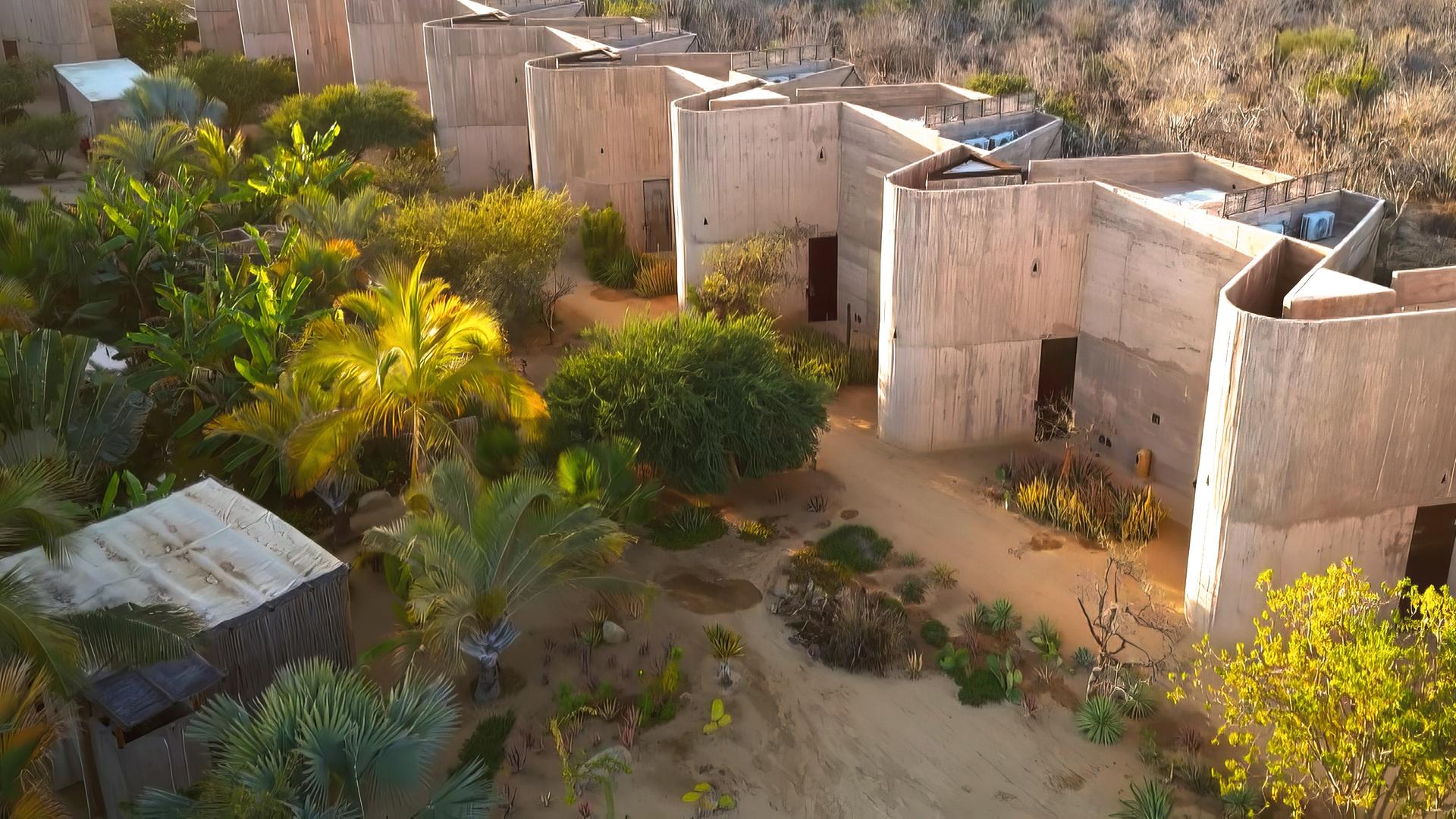 Luftbild: Einer Reihe von modernen, rechteckigen Gebäuden steht in einer trockenen, bewachsenen Landschaft mit Büschen und Bäumen.
