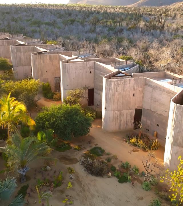 Luftbild: Einer Reihe von modernen, rechteckigen Gebäuden steht in einer trockenen, bewachsenen Landschaft mit Büschen und Bäumen.