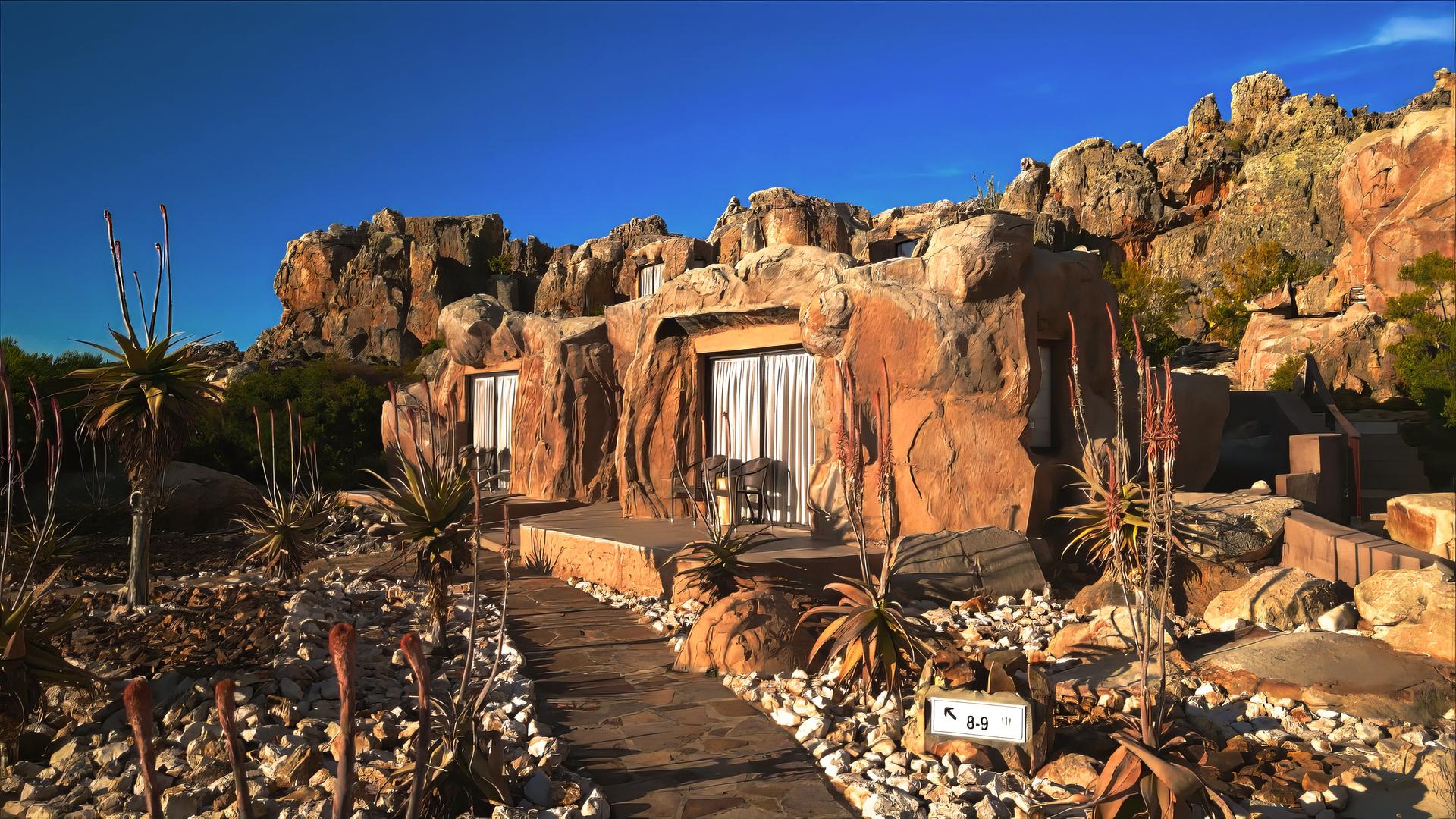 Inmitten von Felsen liegen drei Terrassen mit den Eingängen zu Höhlenzimmern. Davor ist ein Steingarten angelegt.