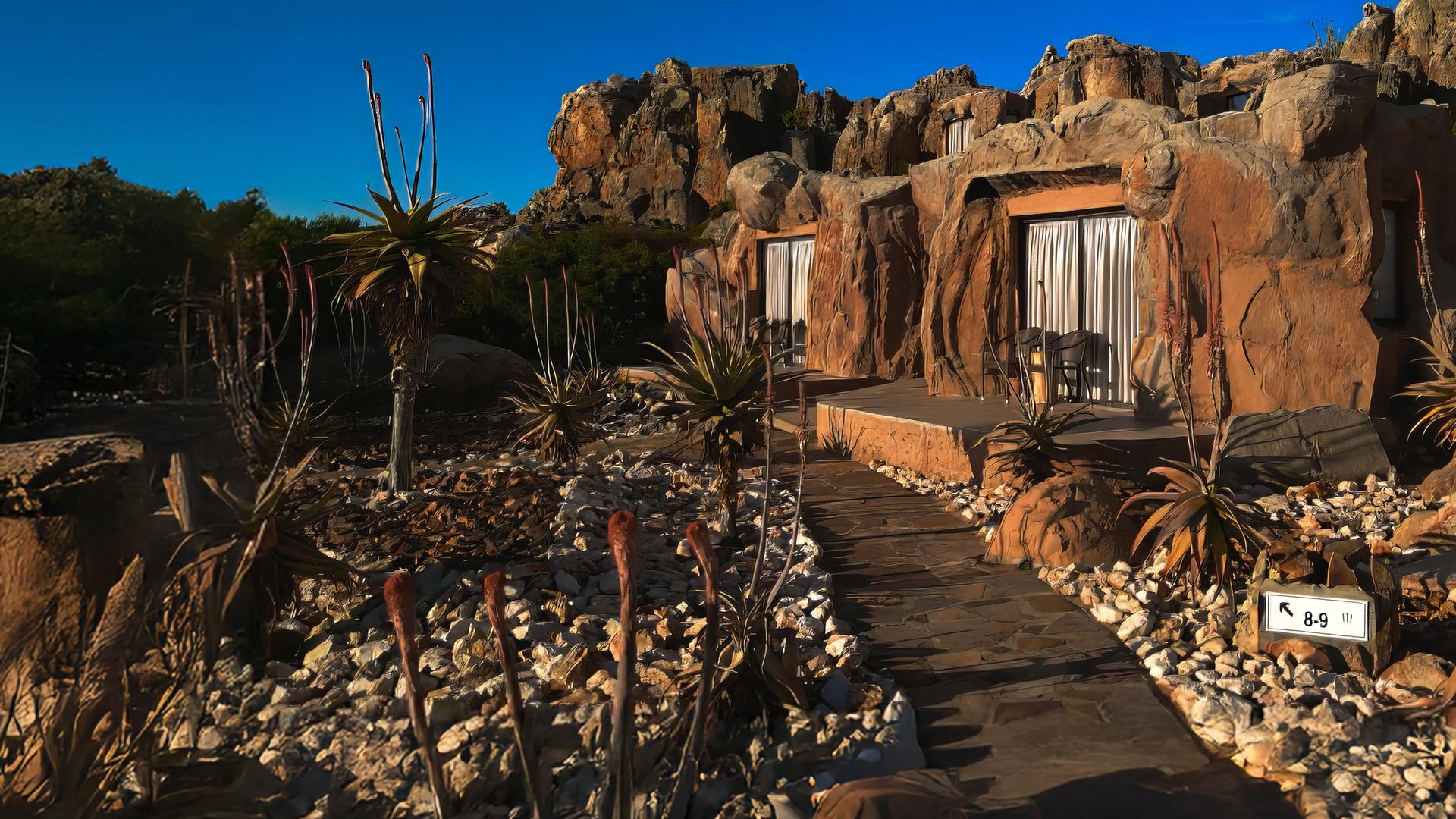 Inmitten von Felsen liegen drei Terrassen mit den Eingängen zu Höhlenzimmern. Davor ist ein Steingarten angelegt.