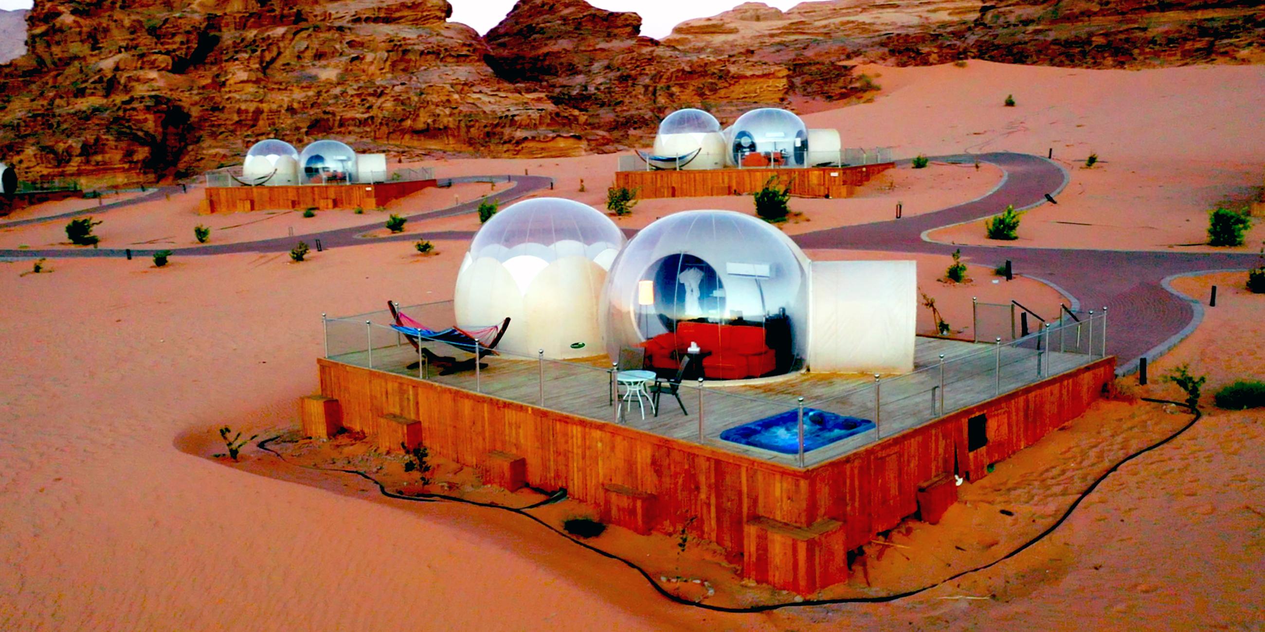 Transparente Kuppeln stehen auf Holzterrassen inmitten einer Wüsten-Berglandschaft.