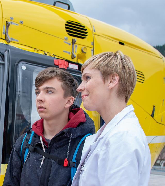Dr. Verena Auerbach (Gundula Niemeyer) steht mit Leon (Tim Marco Rietz) am Rettungshubschauer Michael (Robert Lohr) gegenüber. Verena und Michael lächeln Leon an.