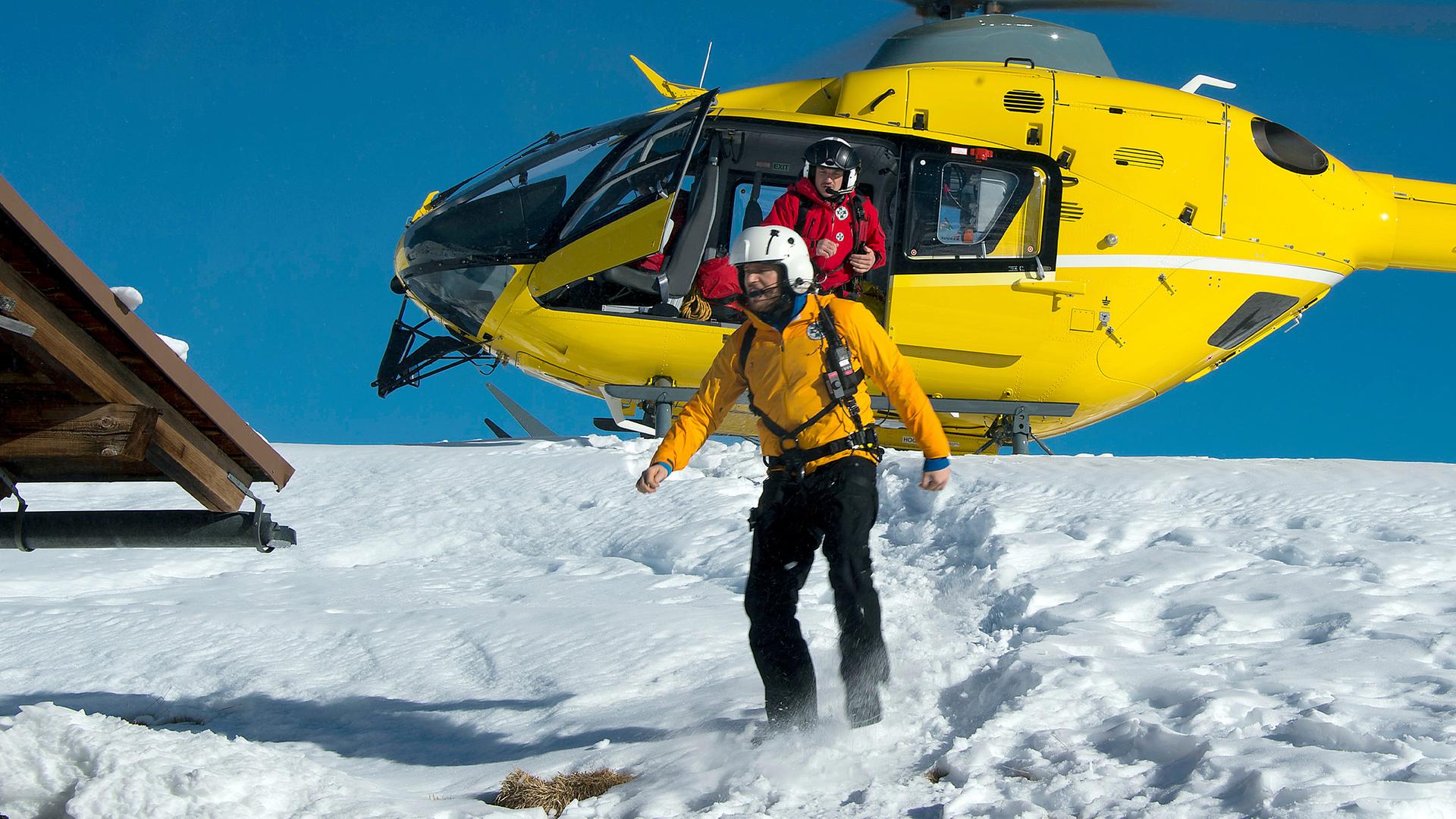Der Rettungshubschrauber steht auf einer schneebedeckten Bergkuppe mit rotierenden Blättern. Tobias (Markus Brandl) springt aus dem Hubschrauber, Markus (Sebastian Ströbel) steht bereits davor. Im Vordergrund steht eine Holzhütte.