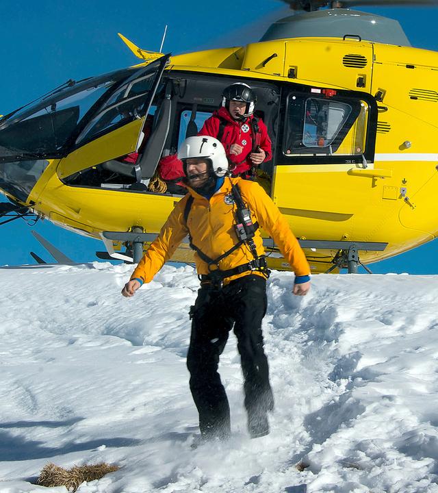 Der Rettungshubschrauber steht auf einer schneebedeckten Bergkuppe mit rotierenden Blättern. Tobias (Markus Brandl) springt aus dem Hubschrauber, Markus (Sebastian Ströbel) steht bereits davor. Im Vordergrund steht eine Holzhütte.