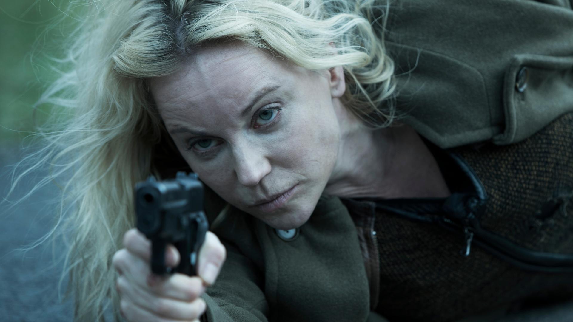 Die Brücke - Das Finale (4): Saga (Sofia Helin) liegt auf der Straße mit ihrer Waffe in der Hand, auf ihren Angreifer zielend.