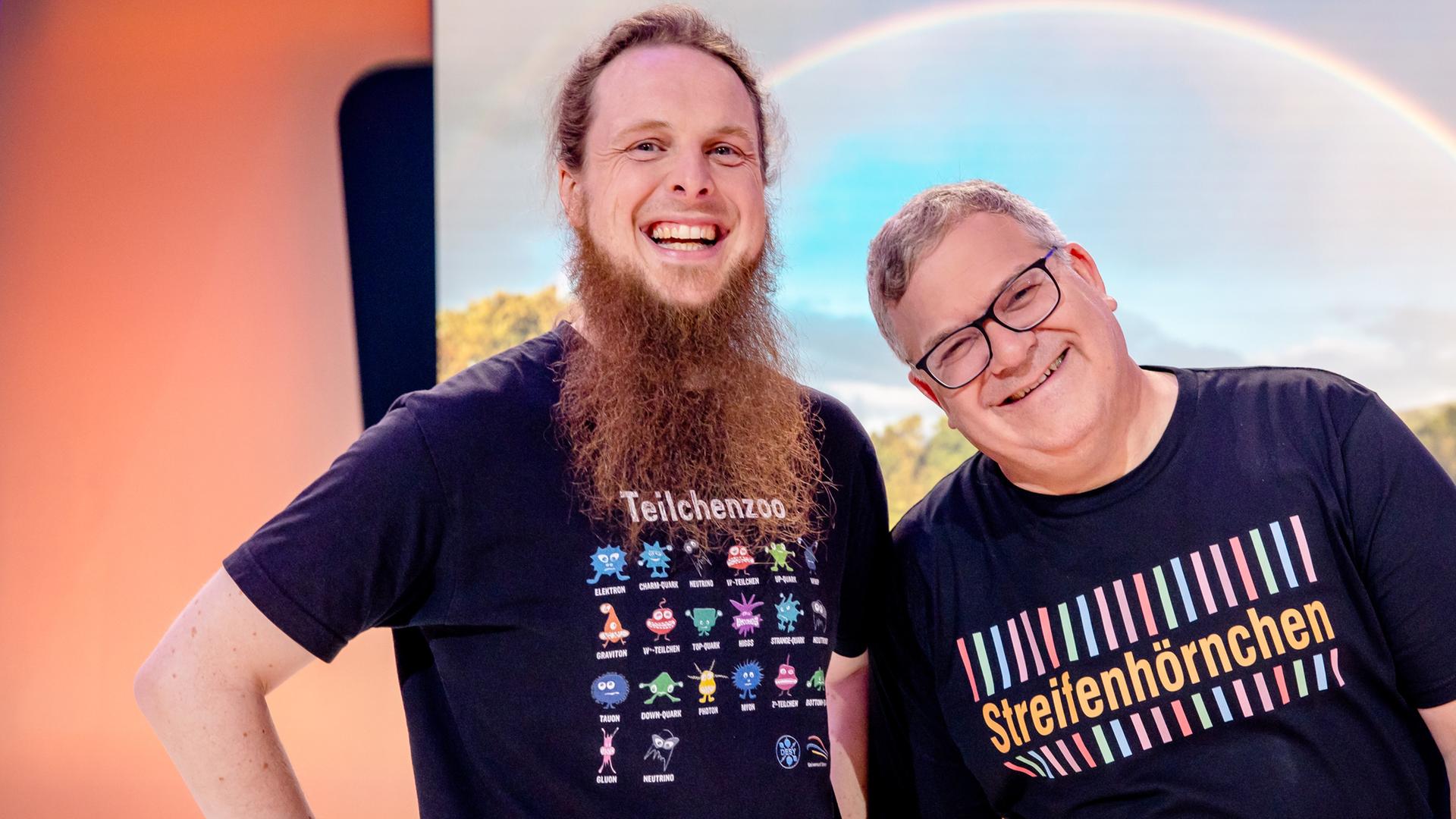 "1, 2 oder 3 - Die bunte Welt der Streifen": Michael Büker und Elton stehen im Studio hinter einem Tisch. Hinter ihnen ist ein großer Regenbogen zu sehen.