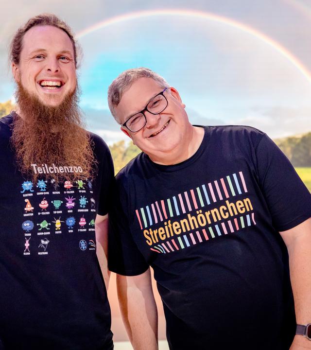 "1, 2 oder 3 - Die bunte Welt der Streifen": Michael Büker und Elton stehen im Studio hinter einem Tisch. Hinter ihnen ist ein großer Regenbogen zu sehen.