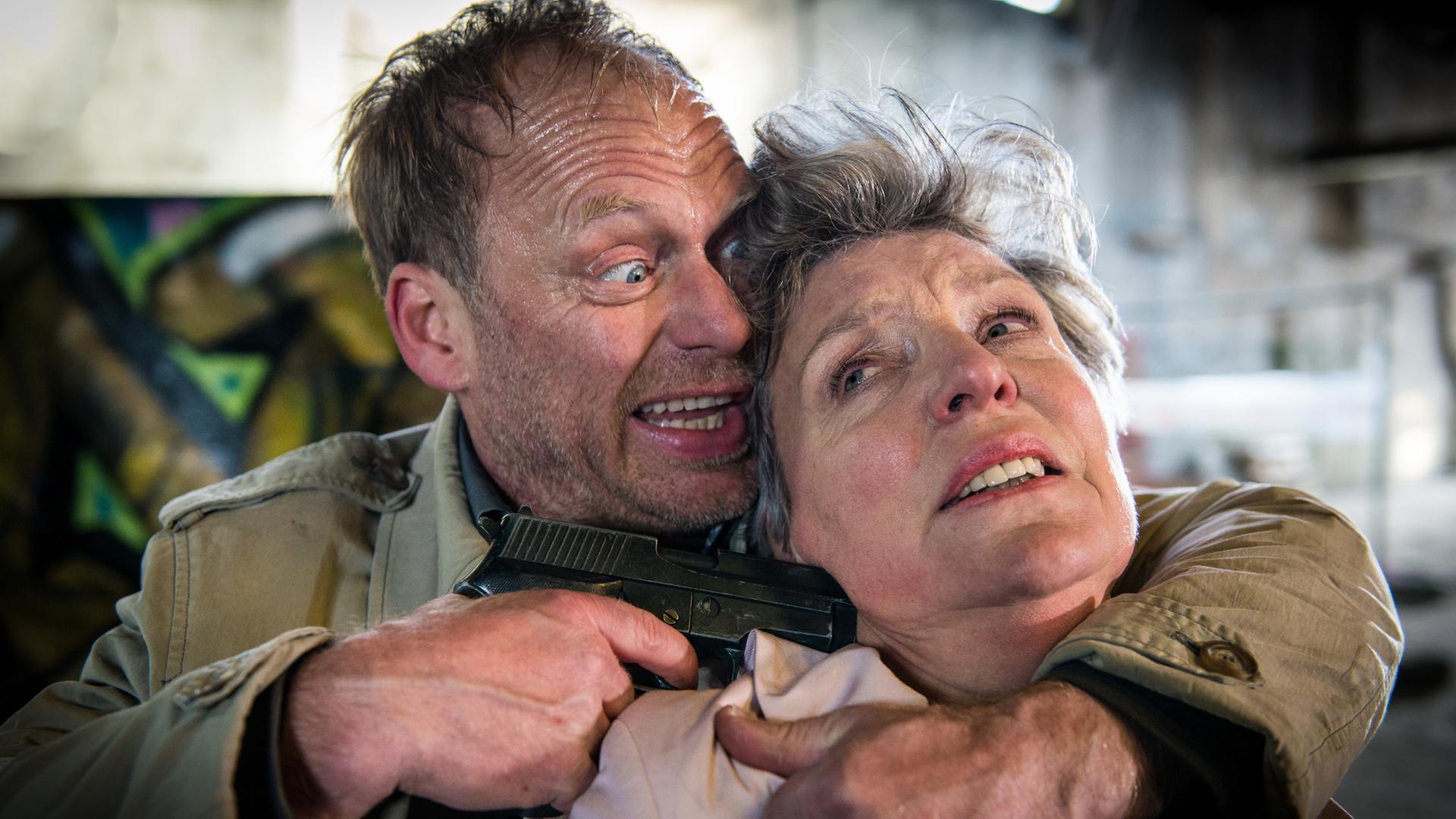 "Notruf Hafenkante - Die falsche Frau": Porträt von Andreas Beckmann (Rainer Strecker), der Marlies Hansen (Peggy Lukac) mit dem linken Arm im Schwitzkasten hält, mit der rechten Hand eine Waffe an den Kopf hält.