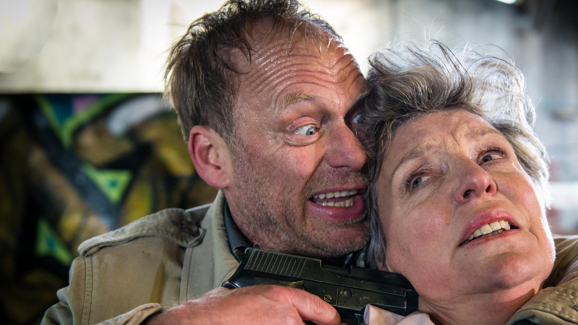"Notruf Hafenkante - Die falsche Frau": Porträt von Andreas Beckmann (Rainer Strecker), der Marlies Hansen (Peggy Lukac) mit dem linken Arm im Schwitzkasten hält, mit der rechten Hand eine Waffe an den Kopf hält.