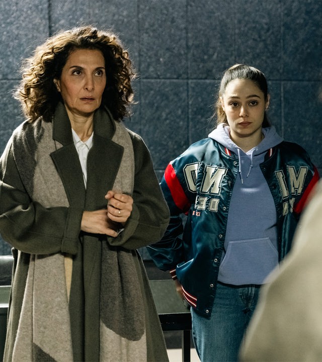 "SOKO Köln - Die Frau auf dem roten Fahrrad": Yasmin Barani (Proschat Madani) steht neben Amira Mahdi (Aylin Ravanyar) vor einer dunkelgrauen Wand mit Fliesenmuster. Sie blickt angespannt nach oben. Amira hat die Arme in die Hüften gestemmt und sieht ernst zu Lilly Funke (Tatjana Kästel), die ihr gegenüber steht, mit dem Rücken zur Kamera.