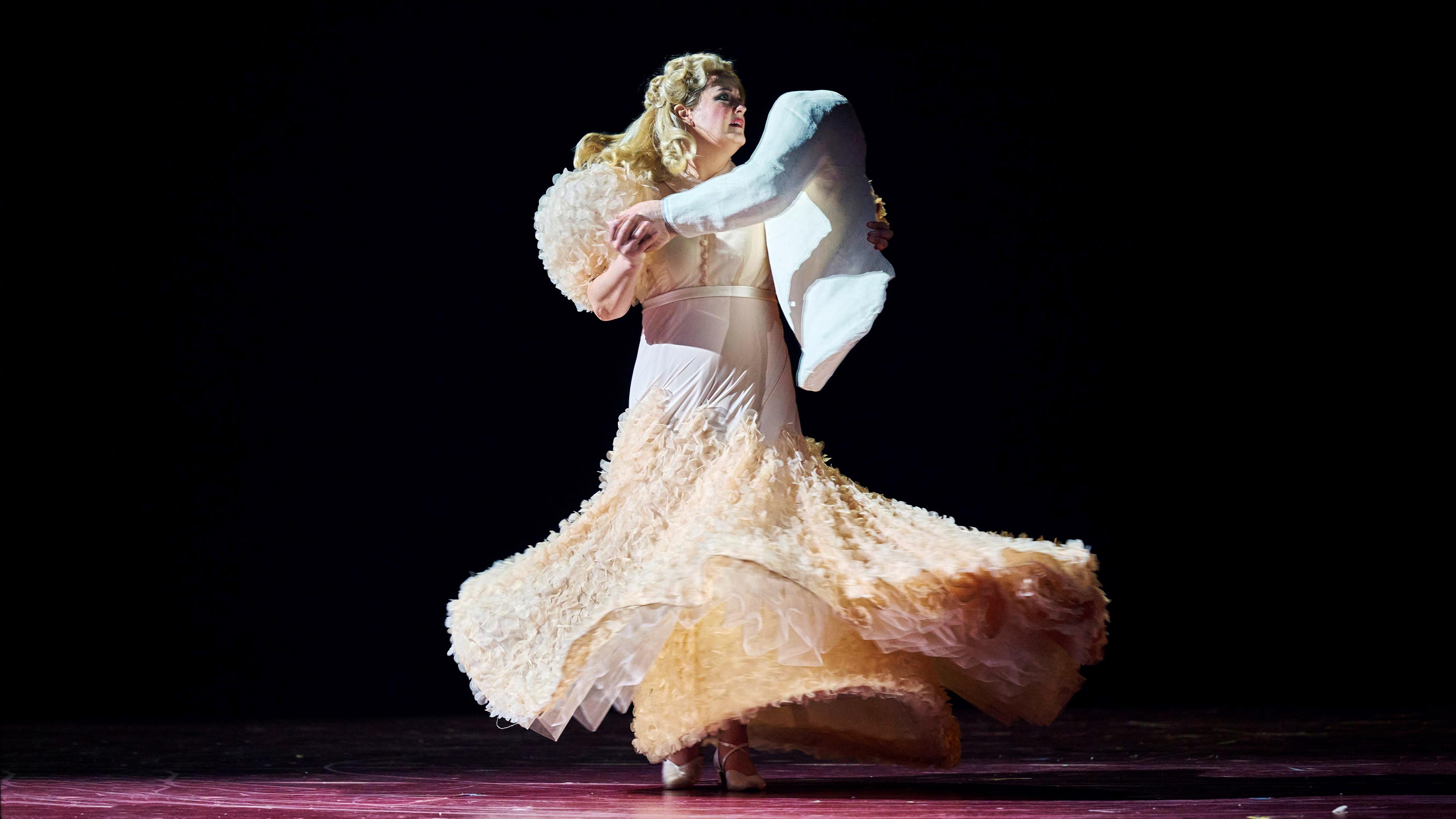"Richard Strauss: Die Frau ohne Schatten": Tanzende Frau in einem champagnerfarbenen Abendkleid. Als Tanzpartner hält sie eine Puppe in Form eines Oberkörpers in den Armen.