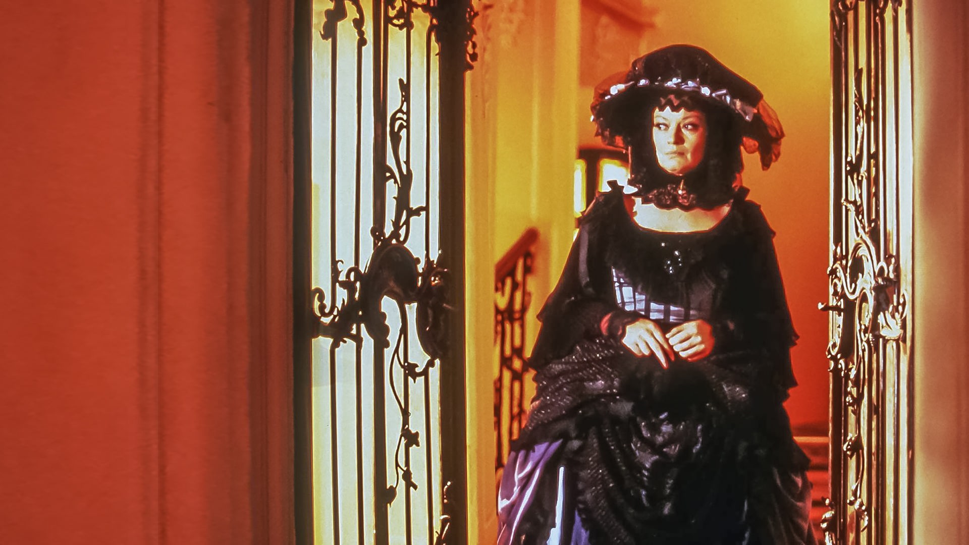 Die skeptische Sorgenfee (Jana Brejchová) steht im Rahmen einer geöffneten, reich verzierten Tür. Beide Türflügel sind geöffnet, hinter ihr erstrahlt warmes Licht. Sie tritt ins Dunkle hinaus.