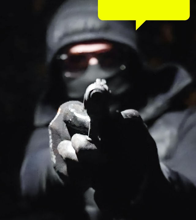 In der Dunkelheit hält ein vermummter Mann eine Waffe in den Händen und zielt damit geradeaus.