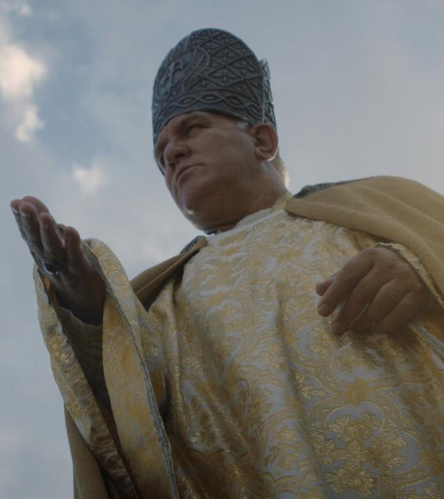 Ein Mann in der Kleidung eines Bischofs streckt verheißungsvoll die Hand aus.