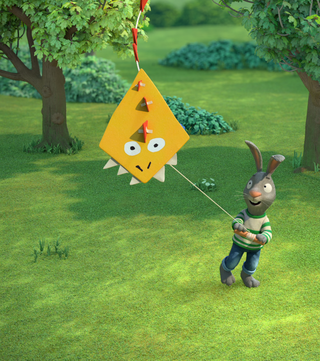 Pip lässt einen gelben Drachen steigen. Er ist im Park und hält ihn an einer Schnur.