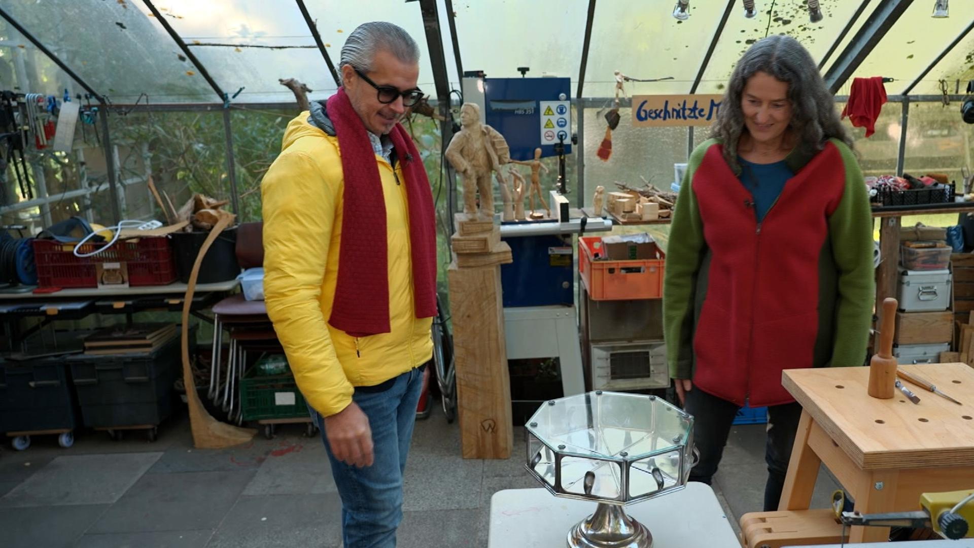 Anaisio Guedes steht neben einer Holzschnitz-Künstlerin und präsentiert ein Tortenbuffet.