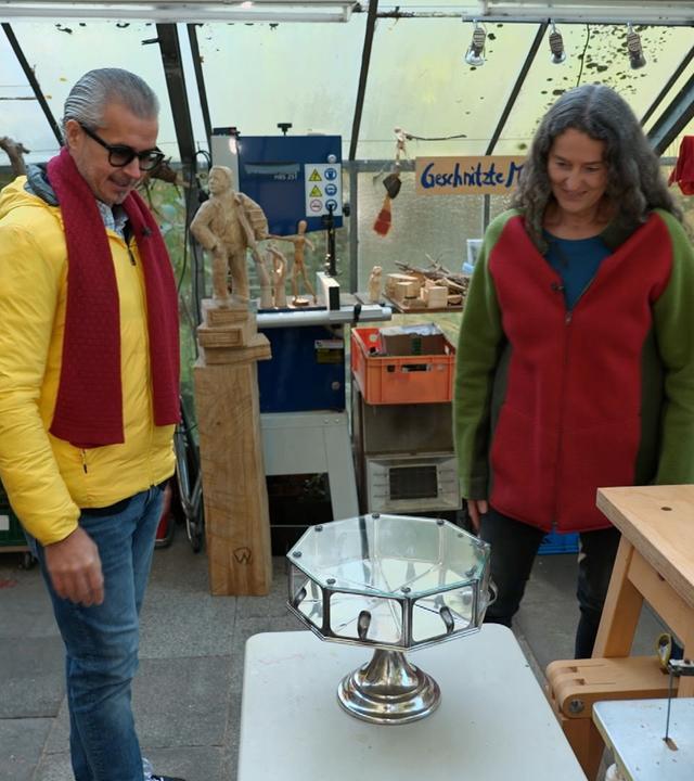 Anaisio Guedes steht neben einer Holzschnitz-Künstlerin und präsentiert ein Tortenbuffet.