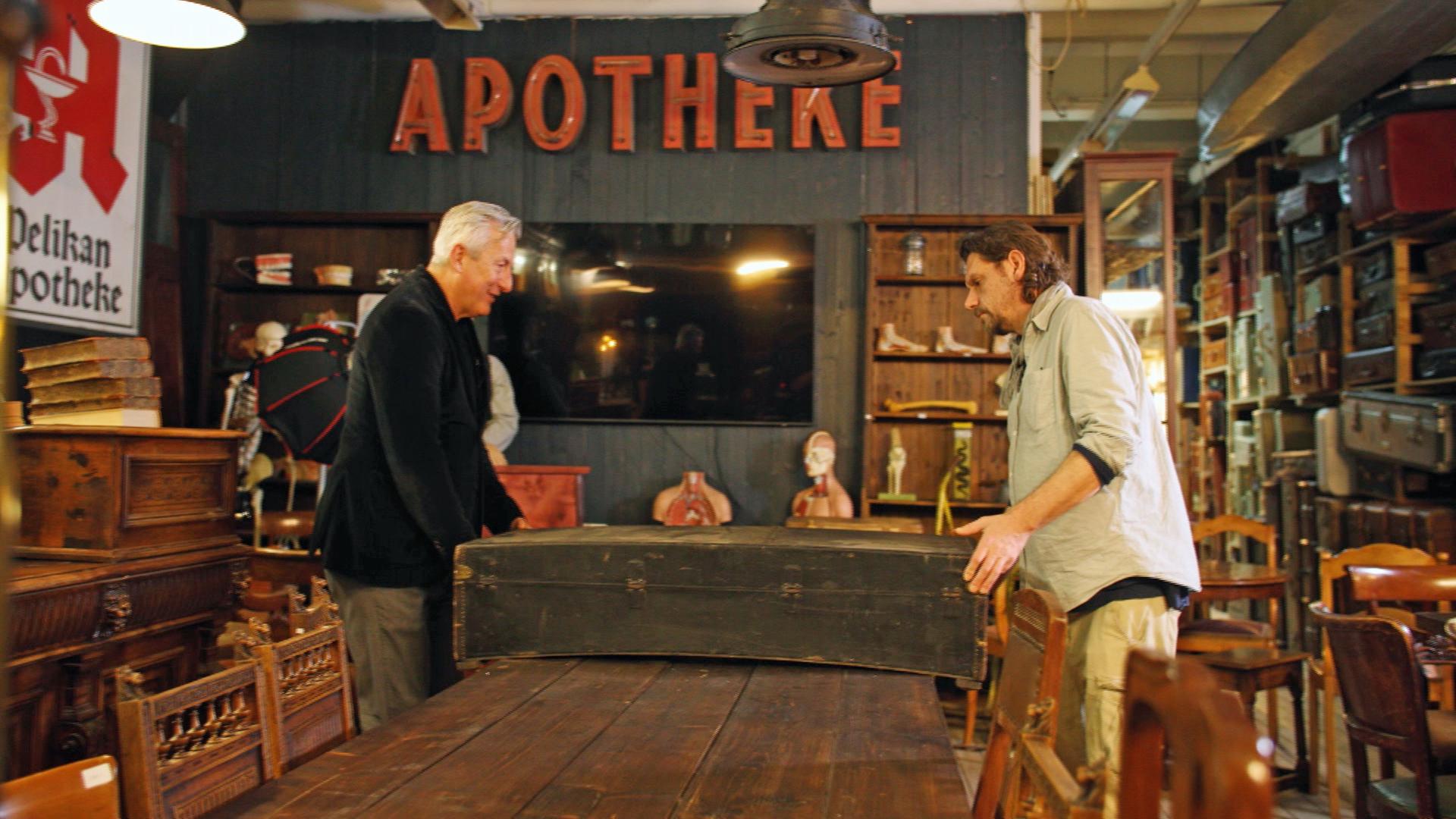 Händler Markus Wildhagen und Handwerker Guido begutachten einen großen, alten Holzkoffer.