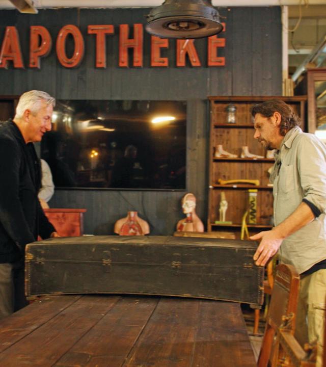 Händler Markus Wildhagen und Handwerker Guido begutachten einen großen, alten Holzkoffer.