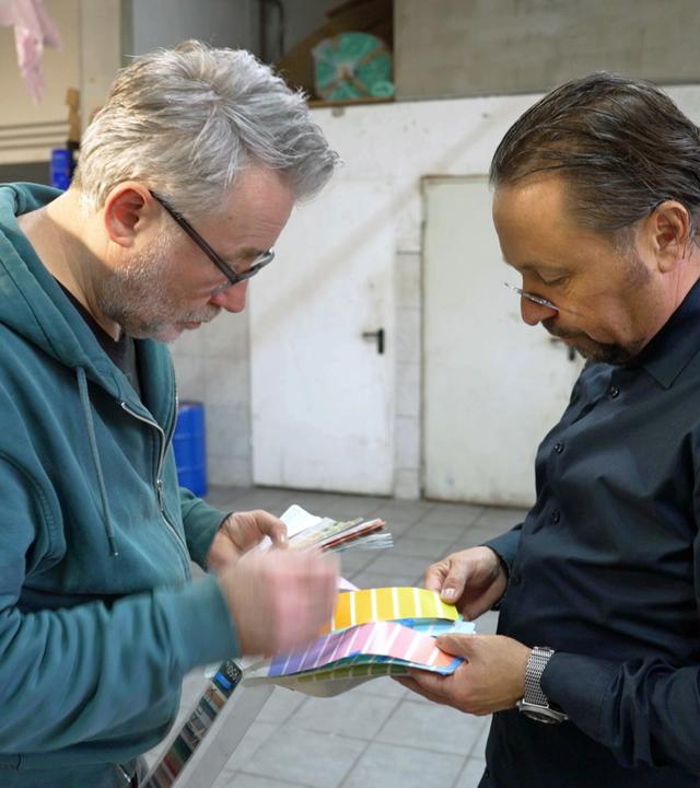 Jan Čížek und Wolfgang Pauritsch schauen sich gemeinsam eine Farbpalette für die neue Farbe ihrer Schachpyramide an.