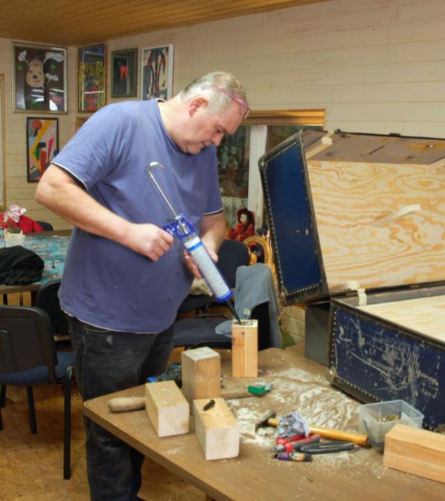 Waldi repariert mit einer Klebepistole einen alten Überseekoffer.