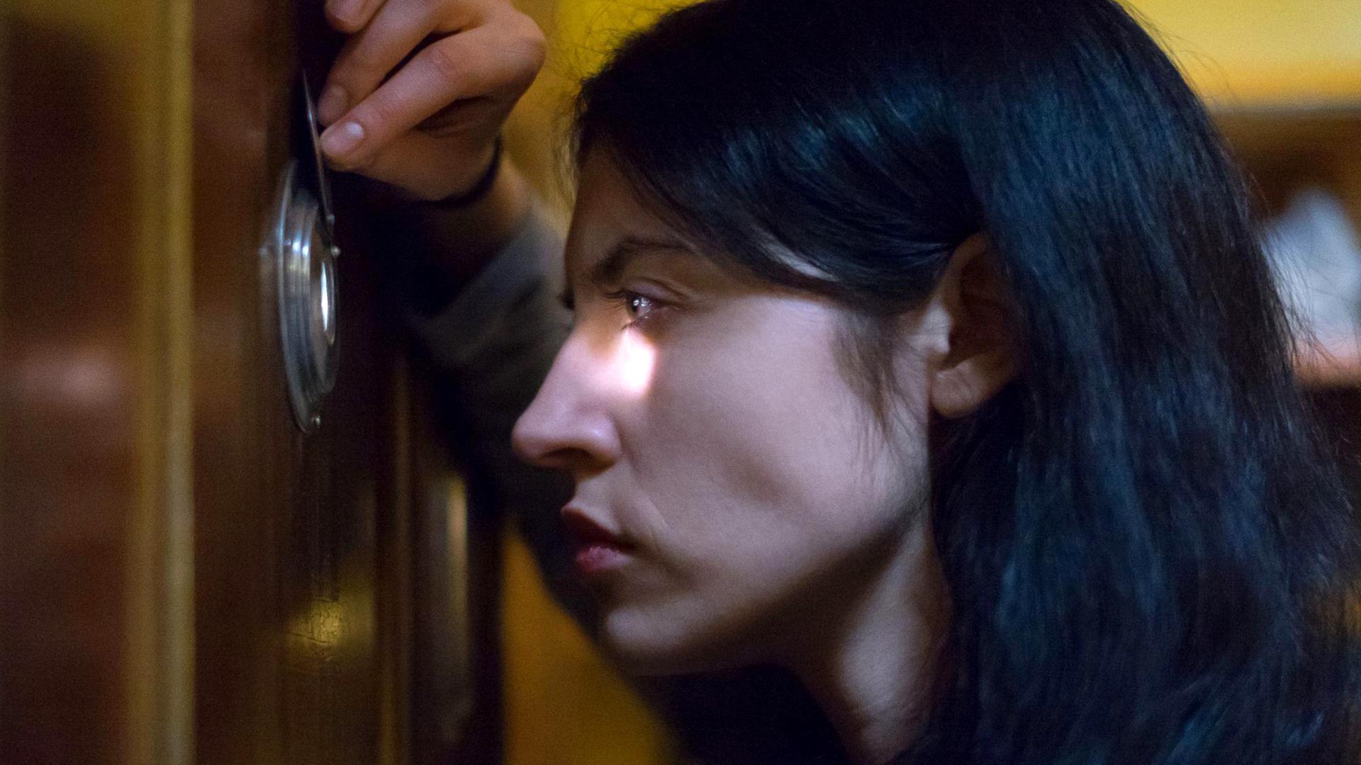 Özge (Violetta Schurawlow) blickt in seitlicher Großaufnahme durch einen Türspion.