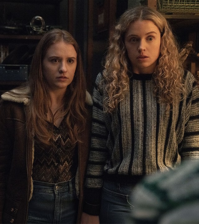 "Extraordinary - Die Jen-Show": Jen (Máiréad Tyers) und Carrie (Sofia Oxenham) stehen in einem Raum mit hohen Regalen und blicken schockiert geradeaus.