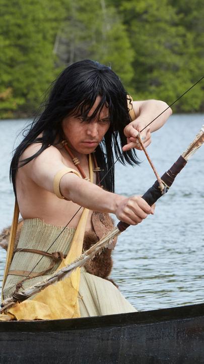 "Die Kanada-Saga - Pioniere und Abenteurer": Spielszene: Häuptling Maquinna (Darsteller unbekannt) vom Volk der Mowachaht sitzt in einem Boot und zielt mit Pfeil und Bogen in Richtung Wasser.