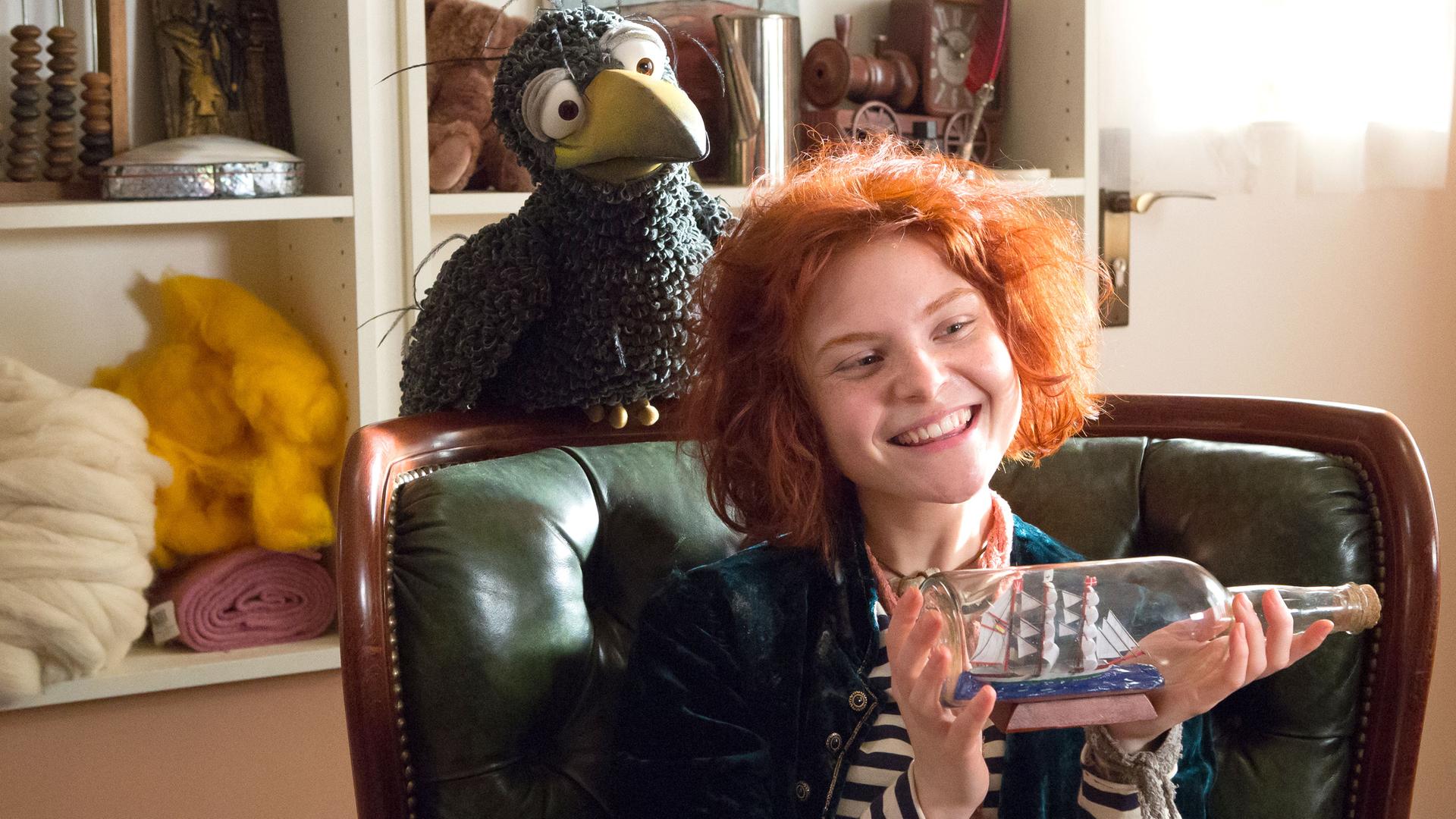 Rudi hockt auf der Lehne eines Sessels, auf dem Klabauterfrau Karli sitzt und ein Buddelschiff in den Händen hält. Beide schauen frech in den Raum.