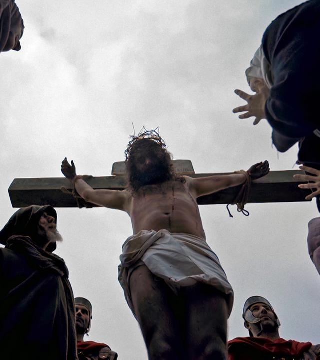 Nachgestellte Szene. Ein Mann mit Dornenkrone am Kreuz, umgeben von einer Menschenmenge. Hinter dem Kreuz stehen römische Wachmänner.