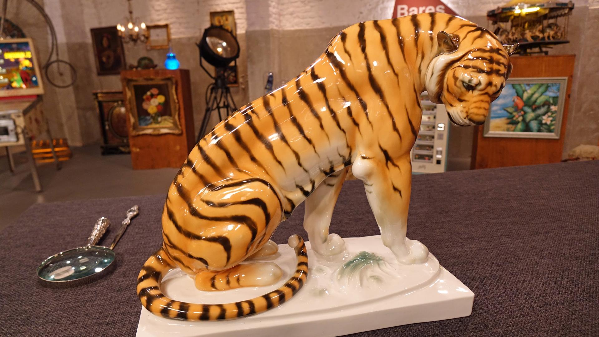 Großer Porzellantiger in Streckhaltung mit nach vorne geneigtem Kopf auf einem weißen Sockel.