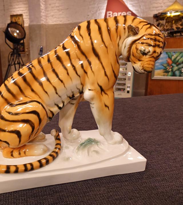 Großer Porzellantiger in Streckhaltung mit nach vorne geneigtem Kopf auf einem weißen Sockel.