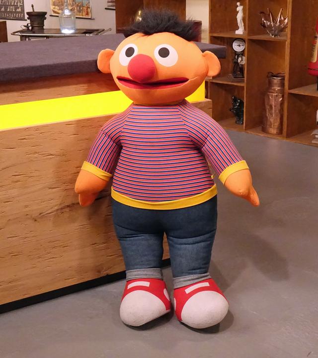 "Ernie" aus der Sesamstrasse als große Stoffpuppe vor dem Tresen im Expertisenraum.