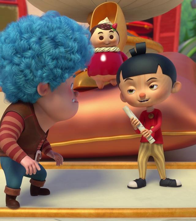 Luzio und Törtchen hören Pinocchio zu, der ein zusammengerolltes Papier in der Hand hält und selbstbewusst schaut. Törtchen steht auf einer großen Kissen-Skulptur im Hintergrund.