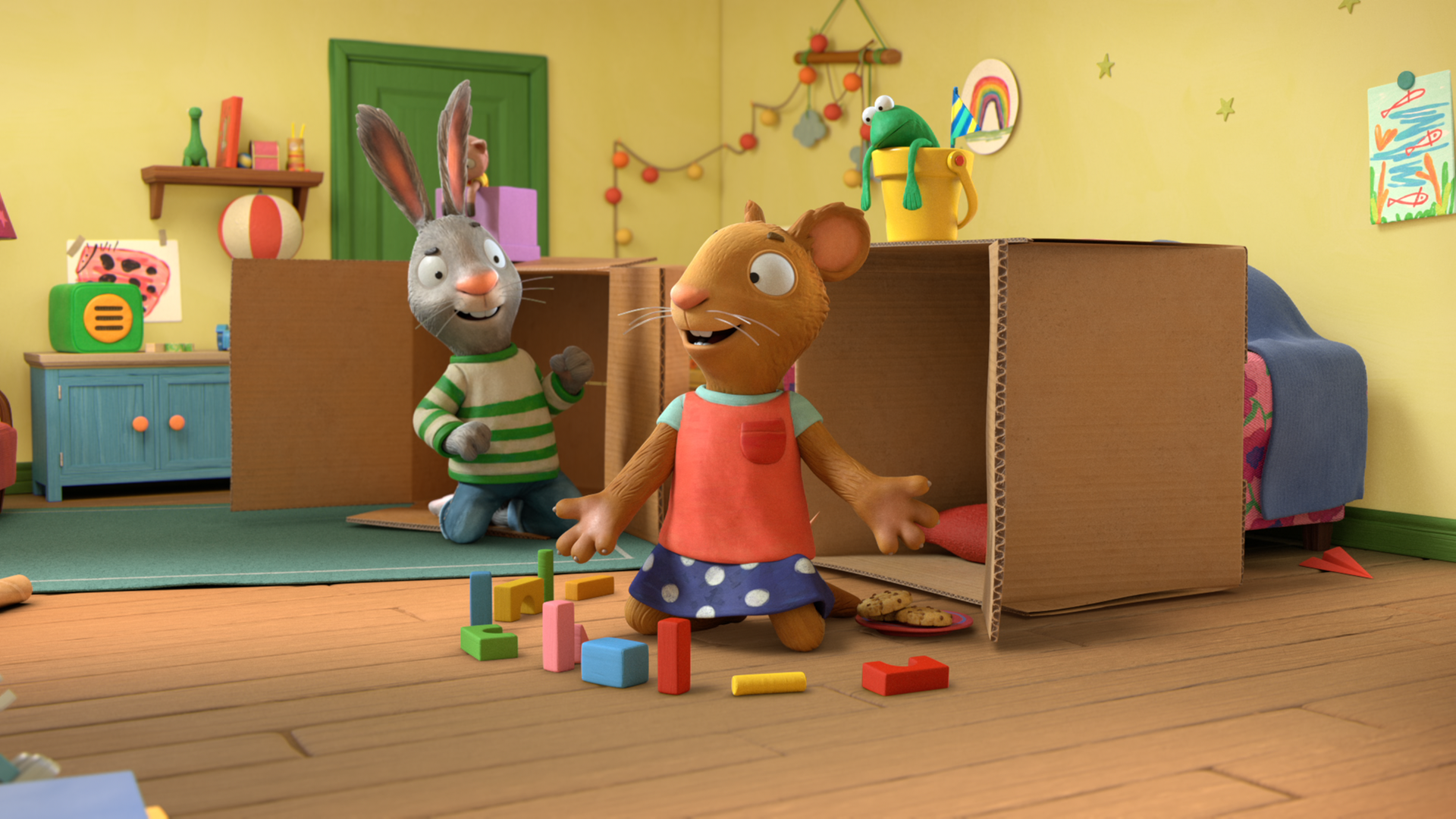 Pip und Posy sind im Kinderzimmer und knien jeweils vor einem Pappkarton. Vor Posy liegen bunte Bauklötze auf dem Boden. Beide unterhalten sich. Im Hintergrund sieht man eine kleine Kommode mit einem CD-Spieler.
