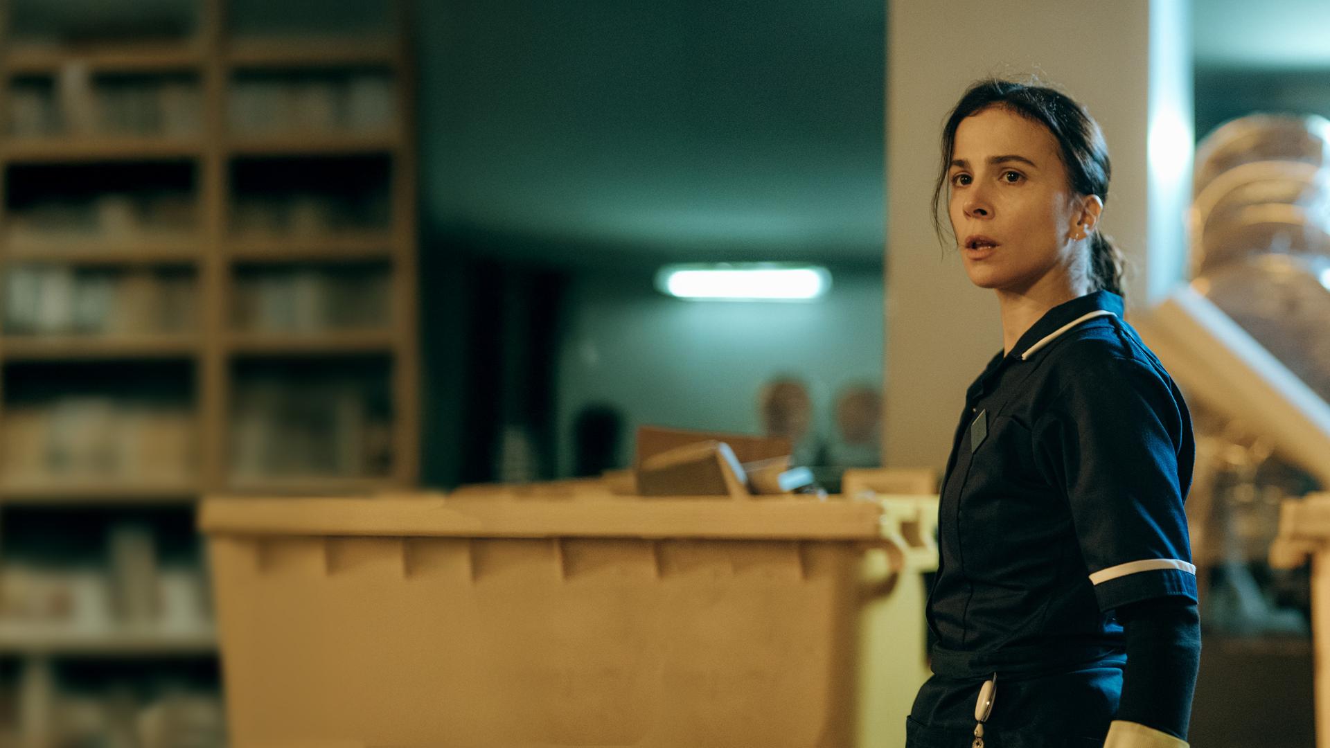 "Serial Cleaner - Die Mission": Teri Marquard (Aylin Tezel) steht in Arbeitskleidung in einem Lagerraum und schaut erstaunt zur Seite.