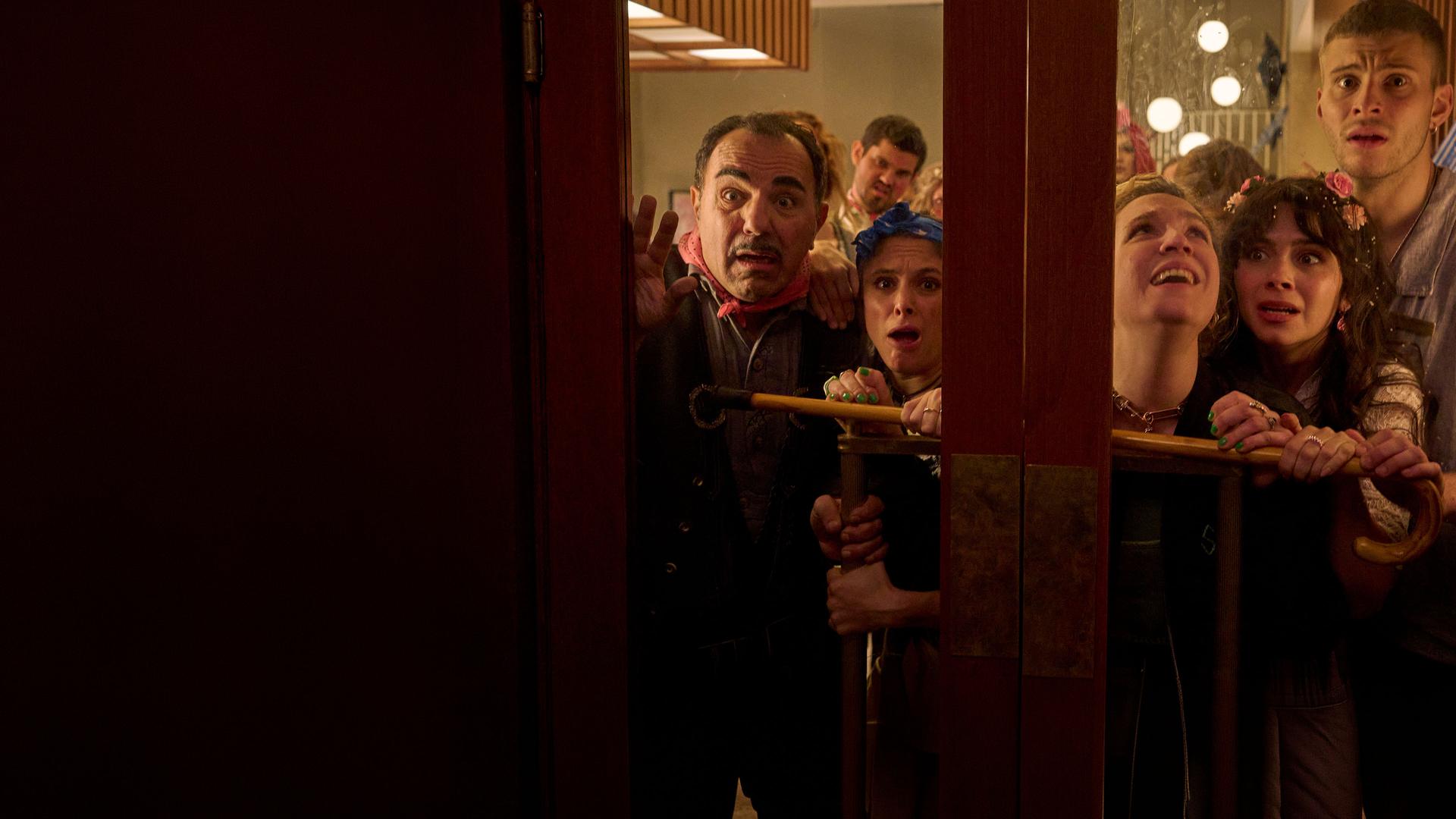 "Nighties - Die Nacht der trinkenden Toten": Die Hotelcrew, Concierge Charles (Adnan Maral), Küchenchefin Franca (Mariananda Schempp), Securitychefin Adriana (Stella Goritzki), Hotelchefin Millie (Tamara Romera Ginés) und Barkeeper Rafael (Ben Felipe), stehen dicht gedrängt hinter einer Glas-Doppeltür. Sie schauen durch die Schreibe und wirken erschrocken. Security-Chefin Adriana hält einen Spazierstock quer gegen die Tür gedrückt.