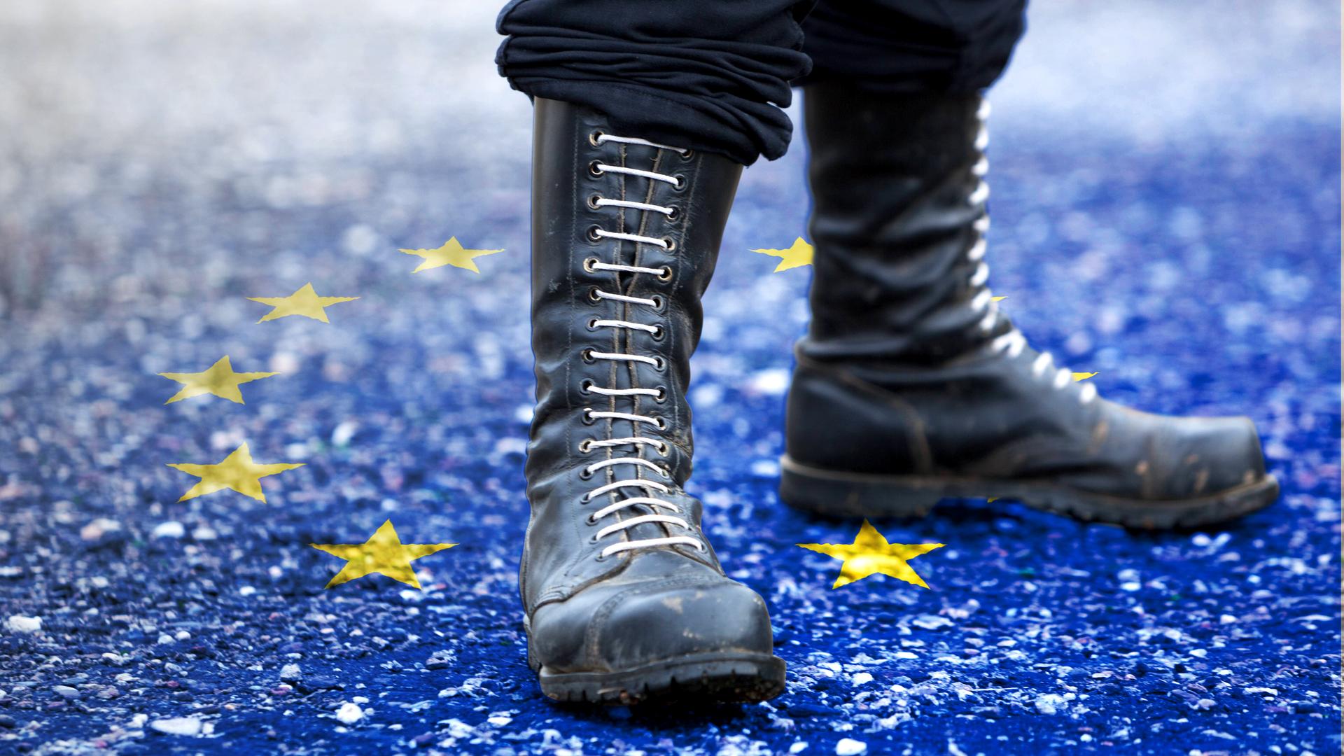 Nahaufnahme von Springerstiefeln mit weißen Schnürsenkeln. Sie stehen auf einer auf dem Boden angedeuteten Flagge der Europäischen Union.