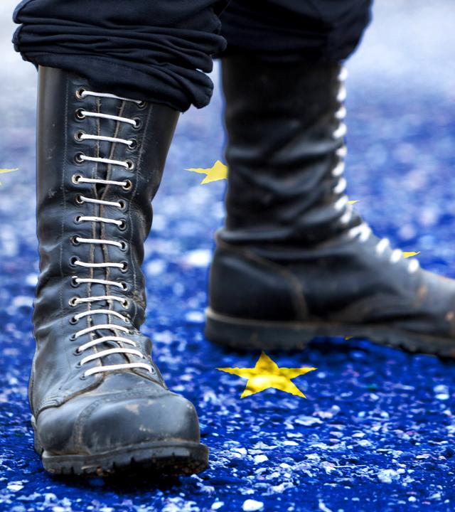 Nahaufnahme von Springerstiefeln mit weißen Schnürsenkeln. Sie stehen auf einer auf dem Boden angedeuteten Flagge der Europäischen Union.