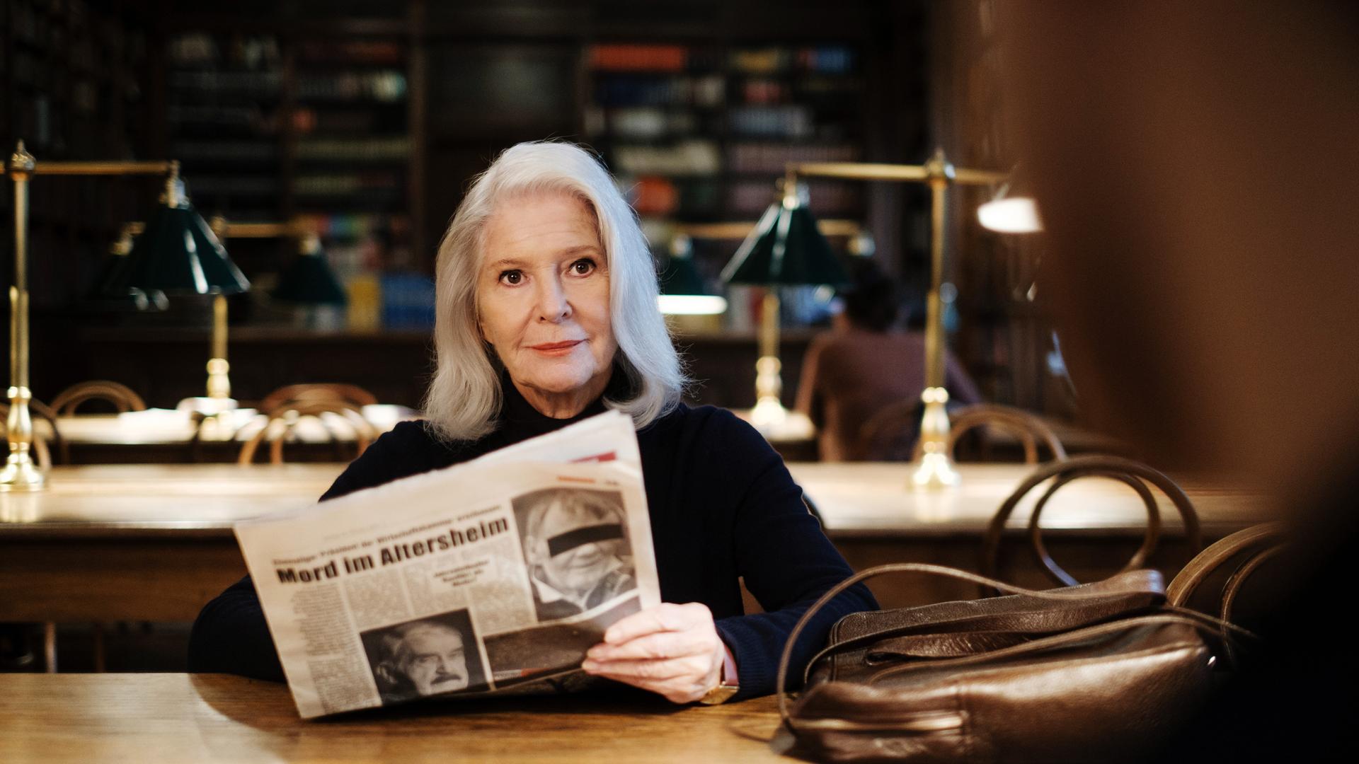 Eine Frau sitzt mit einer Zeitung in einer Bibliothek