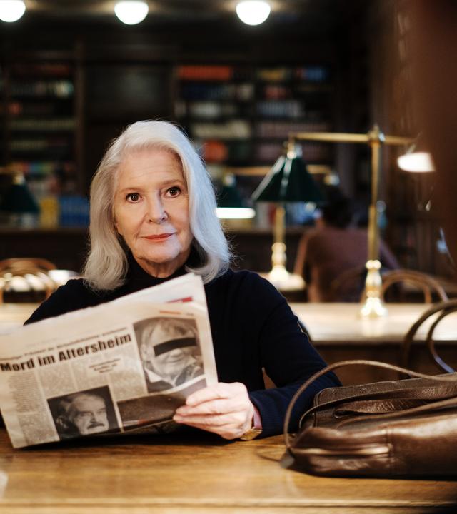 Eine Frau sitzt mit einer Zeitung in einer Bibliothek