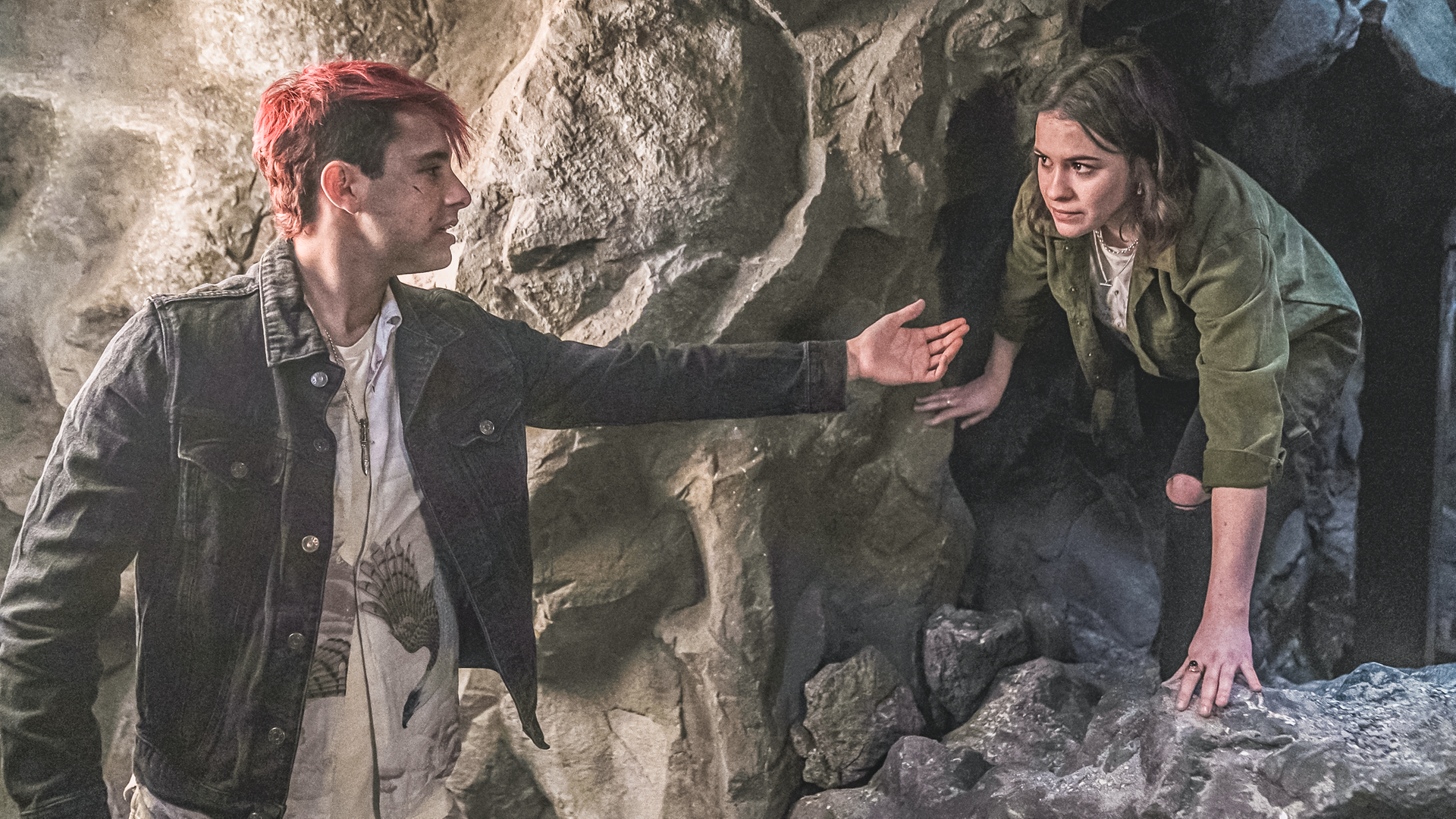 In einer Höhle steht Gabe vor einem Tunnel aus dem Issie gebeugt herauskriecht. Gabe reicht ihr seine ausgestreckte Hand zur Hilfe.