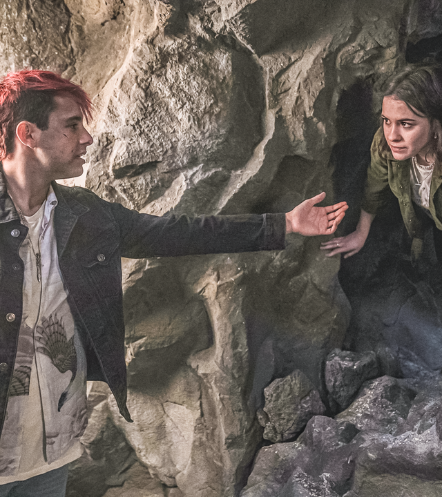 In einer Höhle steht Gabe vor einem Tunnel aus dem Issie gebeugt herauskriecht. Gabe reicht ihr seine ausgestreckte Hand zur Hilfe.