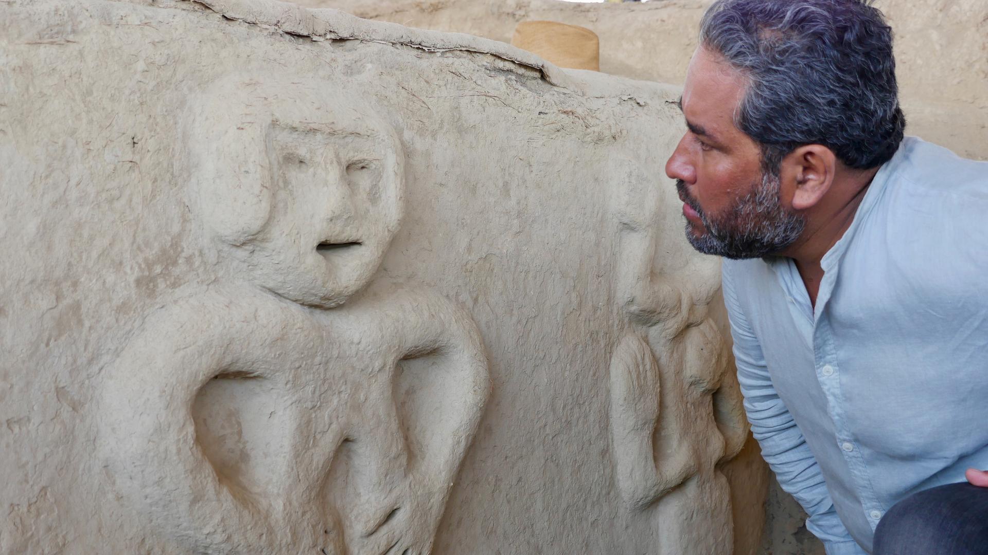 Der Archäologe Sarmiento beugt sich in der Ausgrabungsstätte Vichama zu einer menschenähnlichen Wandfigur aus weißem Kalkstuck, um sie besser zu studieren.