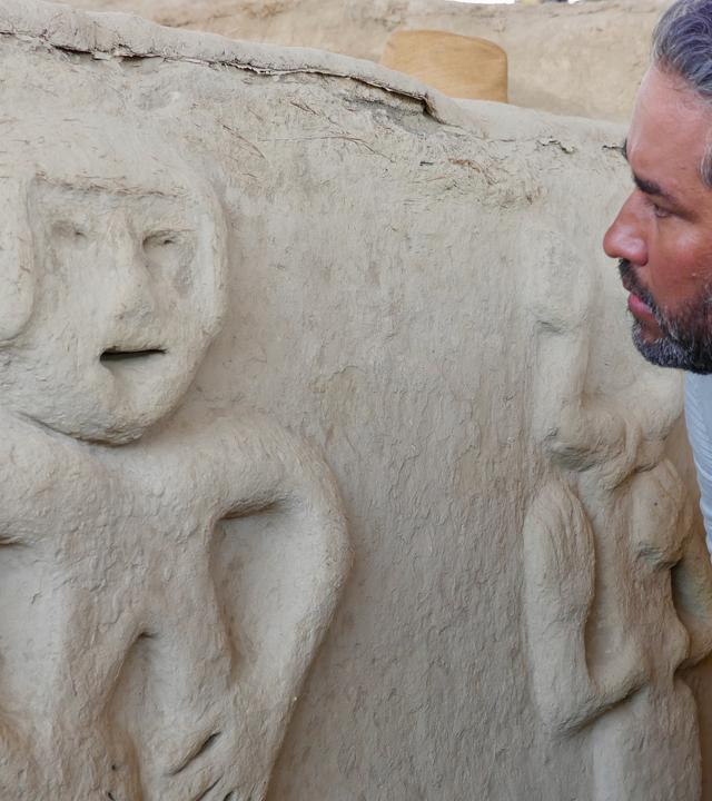 Der Archäologe Sarmiento beugt sich in der Ausgrabungsstätte Vichama zu einer menschenähnlichen Wandfigur aus weißem Kalkstuck, um sie besser zu studieren.