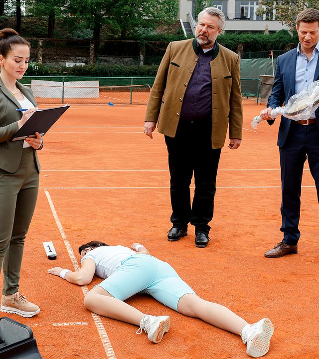 Pathologin Atay (Sevda Polat), Kommissar Stadler (Dieter Fischer) und Kommissar Hansen (Igor Jeftić) stehen um das Mordopfer herum, das bäuchlings auf dem Tennisplatz liegt. Kommissar Hansen hält einen in transparente Folie verpackten Tennisschläger in der Hand.