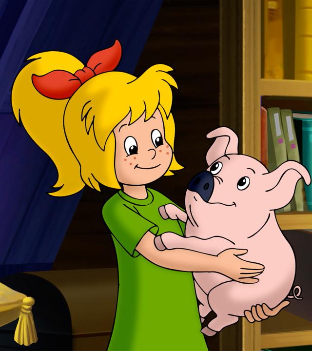 Bibi hält ein kleines Schweinchen, das eine dunkle Schnauze hat, auf den Armen und schaut es stolz an. Neben Bibi, auf einem gelben Kissen, liegt eine Kristallkugel. Auf der anderen Seite von Bibi steht ein Bücherregal.