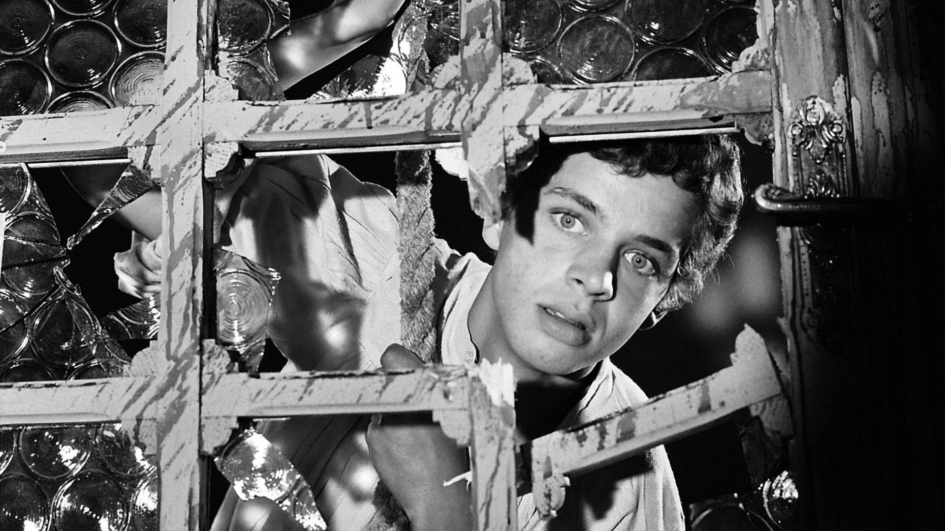 Jim Hawkins steht hinter einem Gitter. In dem Gitter ist ein Loch durch das Jim erstaunt hindurch schaut.