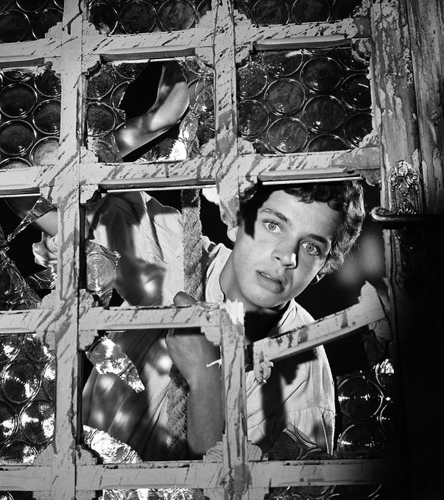 Jim Hawkins steht hinter einem Gitter. In dem Gitter ist ein Loch durch das Jim erstaunt hindurch schaut.